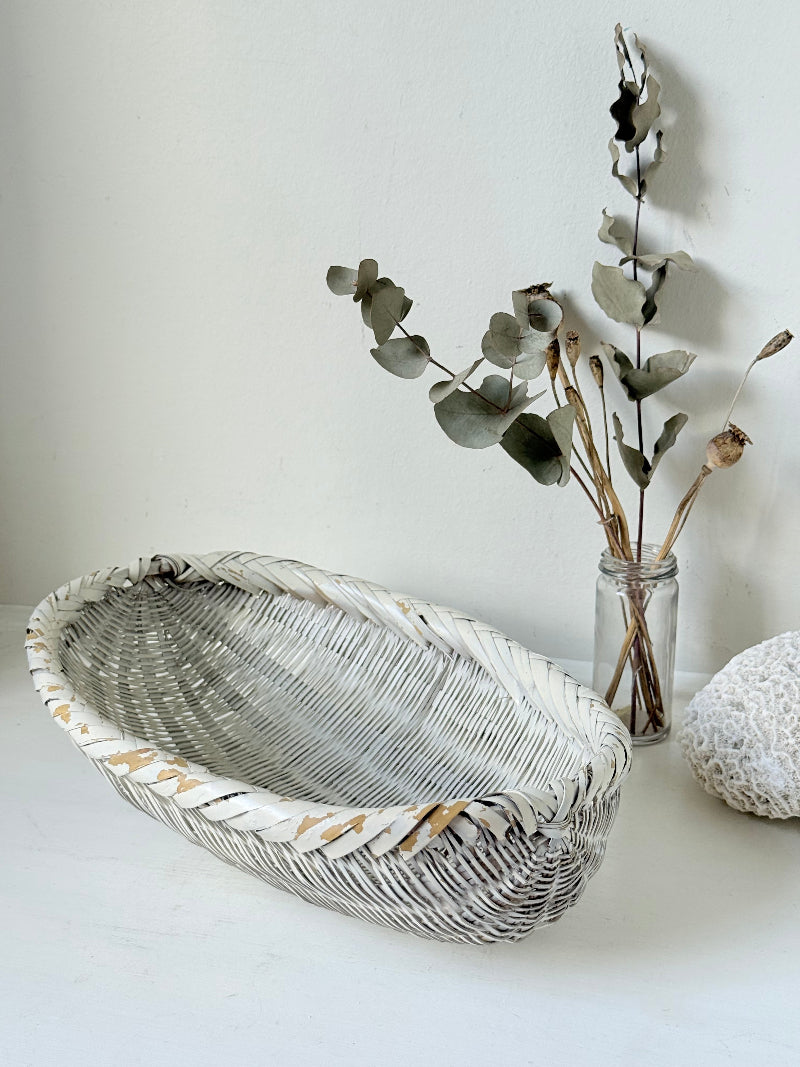 Vintage white chippy wicker basket with oval shape and worn painted finish, photographed on white surface.