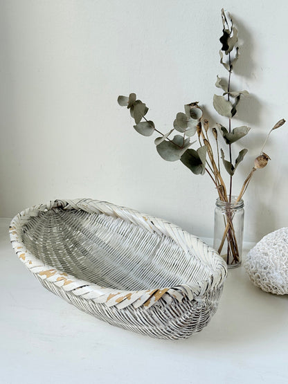 Vintage white chippy wicker basket with oval shape and worn painted finish, photographed on white surface.
