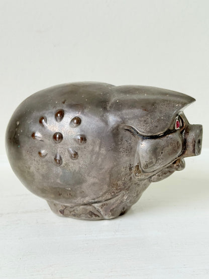 Vintage cast metal piggy bank in the shape of a pig with red painted eyes, photographed on a white surface