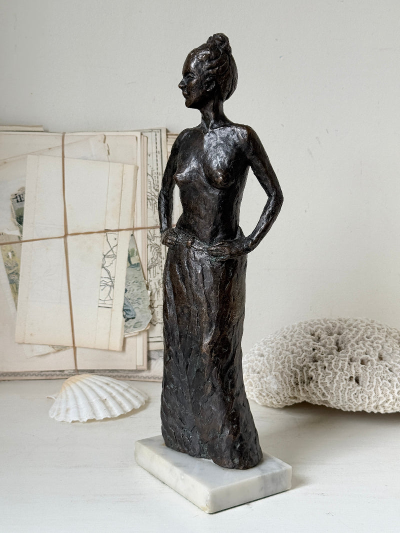 Solid bronze figure of a standing semi nude woman with upswept hair on a white marble base