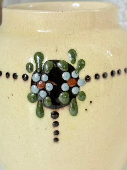 Cream studio pottery decorative pot with raised green floral motif, photographed on a white surface