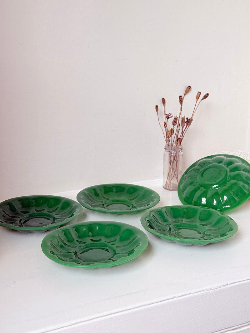 set of five vintage green pressed glass plates with decorative pattern, photographed on a white surface with dried flowers