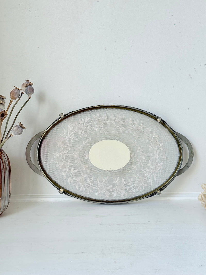Vintage oval metal tray with pierced gallery sides, twin handles, and floral centre, photographed on white surface.