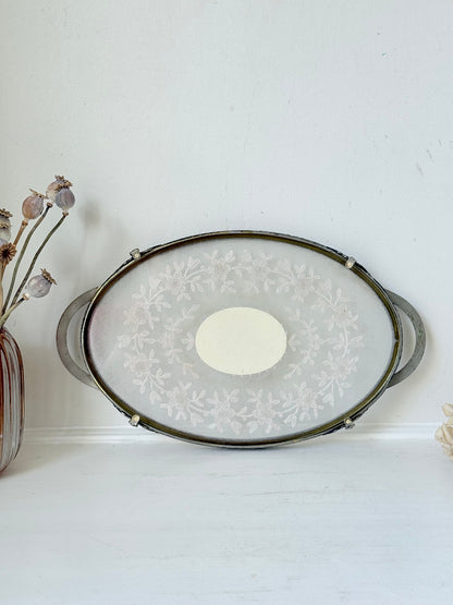 Vintage oval metal tray with pierced gallery sides, twin handles, and floral centre, photographed on white surface.