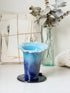 Handmade studio pottery trumpet vase in ombre blue with a frilled rim, photographed on a white surface