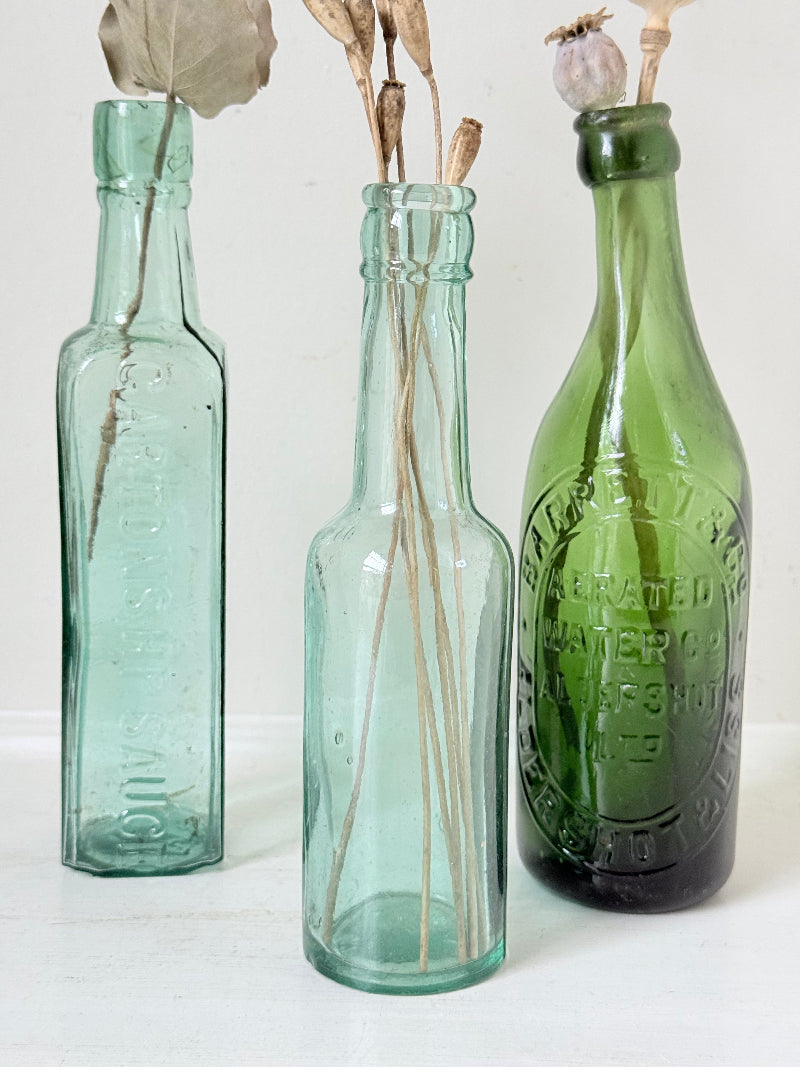 Trio of antique aqua and green glass bottles with embossed lettering, photographed on a white surface
