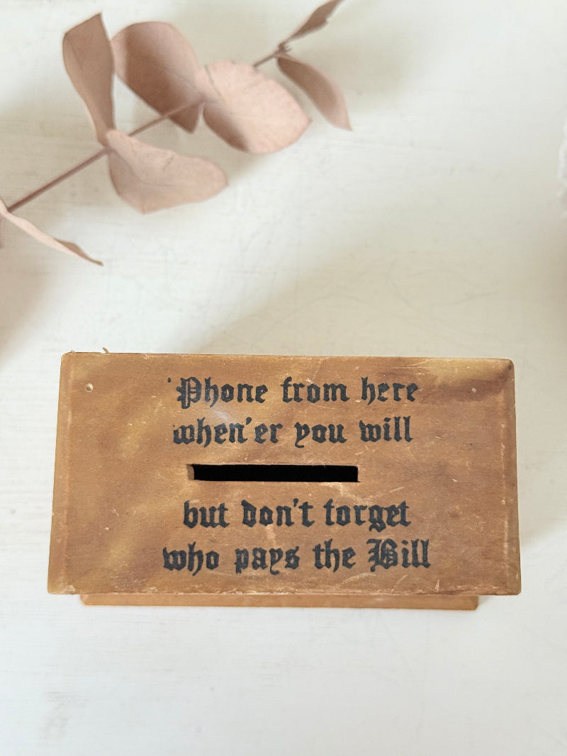 Vintage wooden telephone money box with printed lettering, photographed on a white surface