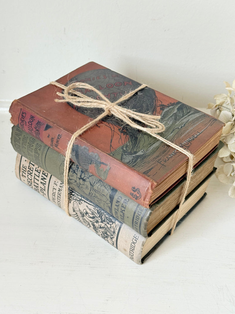 Vintage decorative book bundle in red, olive green and cream tied with twine, photographed on a white surface