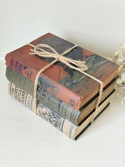 Vintage decorative book bundle in red, olive green and cream tied with twine, photographed on a white surface