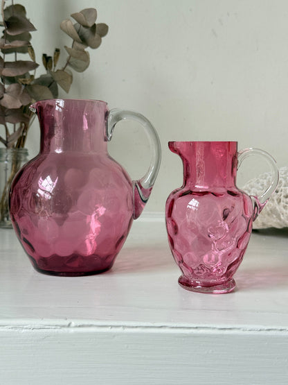 Vintage cranberry glass jugs, a pair with clear handles, photographed on a white surface