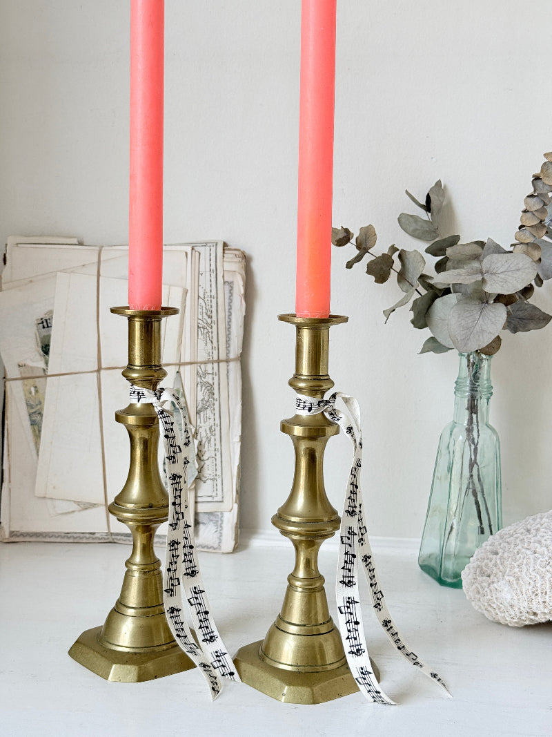 Pair of antique brass candlesticks with turned baluster stems and stepped bases holding coral tapers