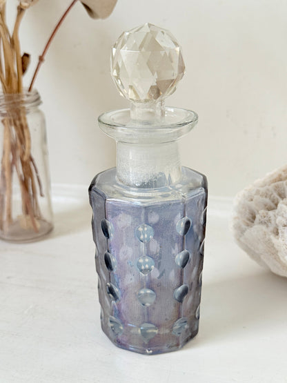 Vintage decagon iridescent glass perfume bottle with raised dot pattern and clear faceted stopper, photographed on a white surface