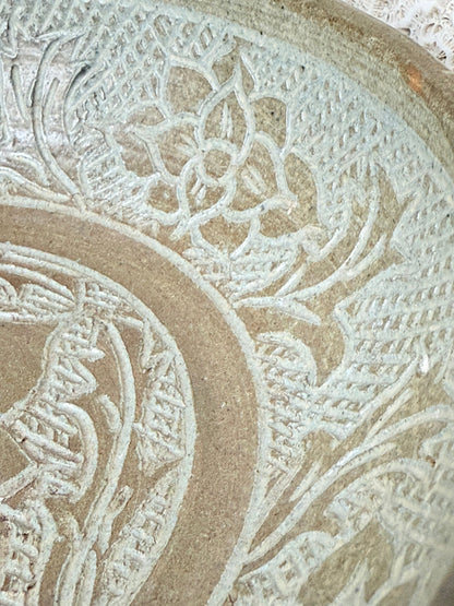 Studio pottery bowl with carved floral and geometric decoration in neutral glaze, photographed on a white surface with a pear inside.