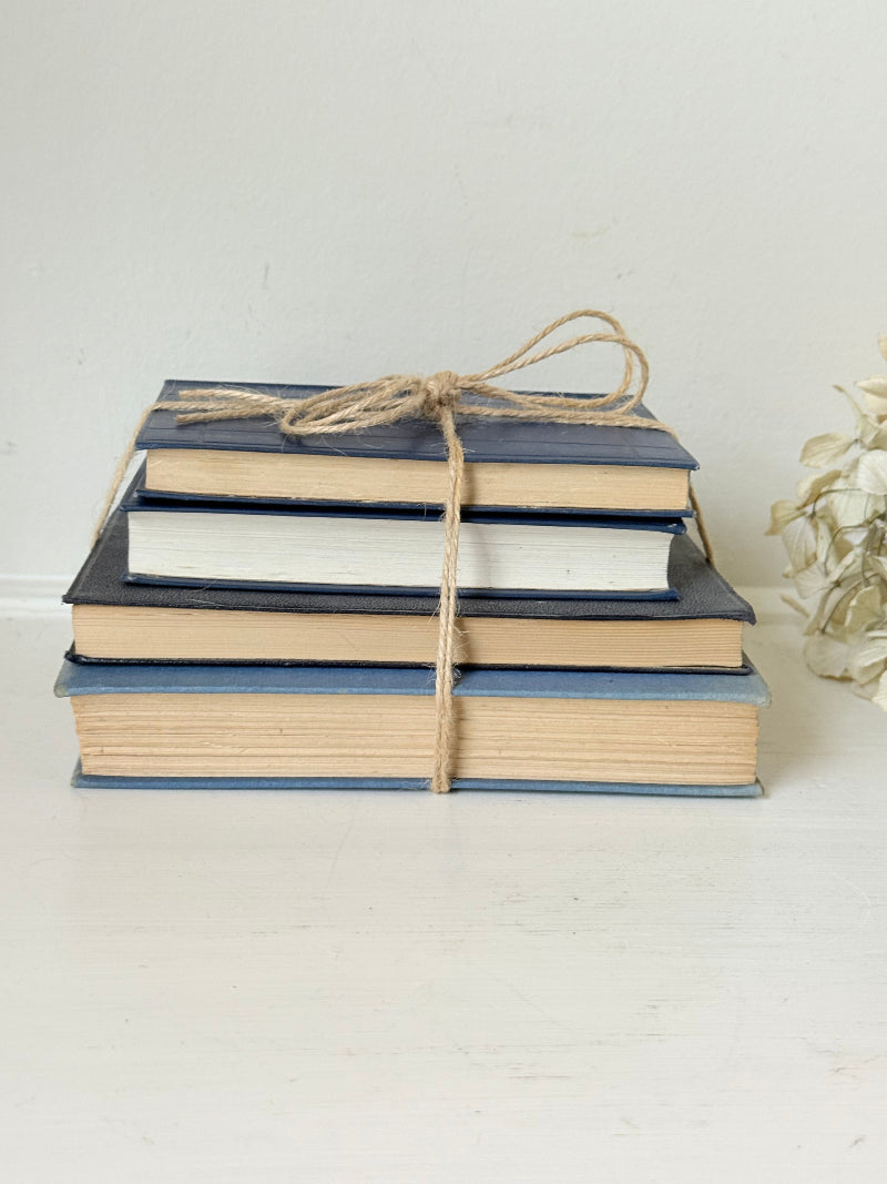 Vintage decorative book bundle in navy, grey, and cream tied with twine, photographed on a white surface