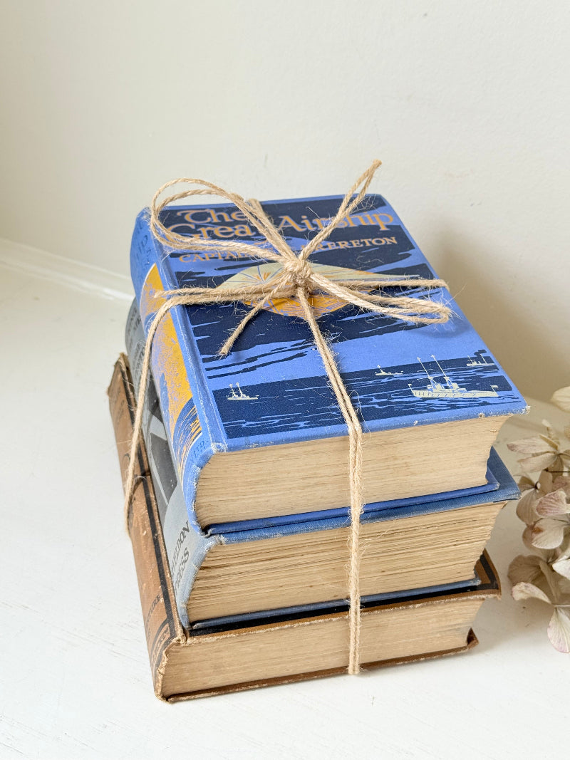 Vintage book bundle in blue, brown, and cream with printed lettering, tied with twine, photographed on a white surface