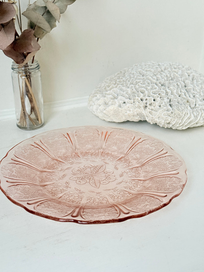 Vintage blush pink pressed glass plate with floral pattern photographed on a white surface