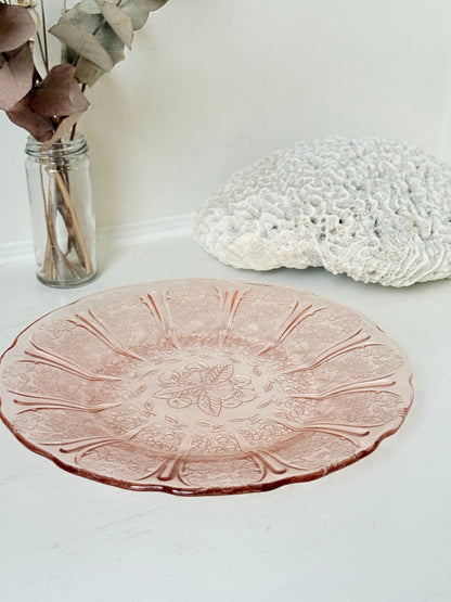 Vintage blush pink pressed glass plate with floral pattern photographed on a white surface