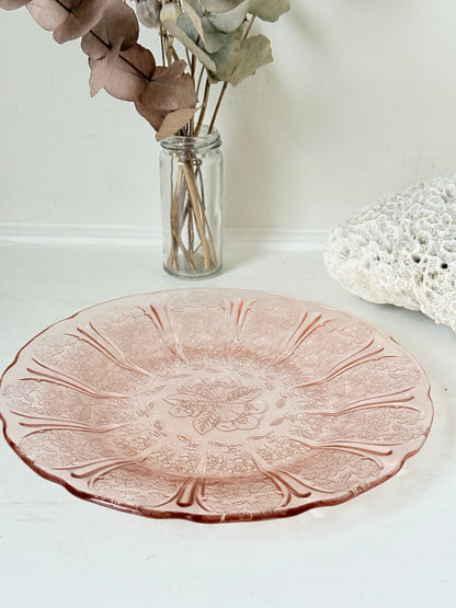 Vintage blush pink pressed glass plate with floral pattern photographed on a white surface