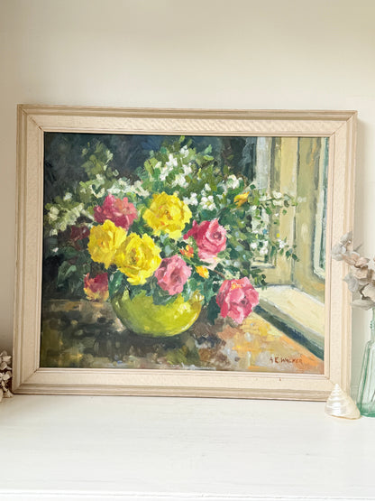 A framed oil painting of a vibrant flower bouquet in a green vase, displayed on a white mantelpiece against a beige wall.