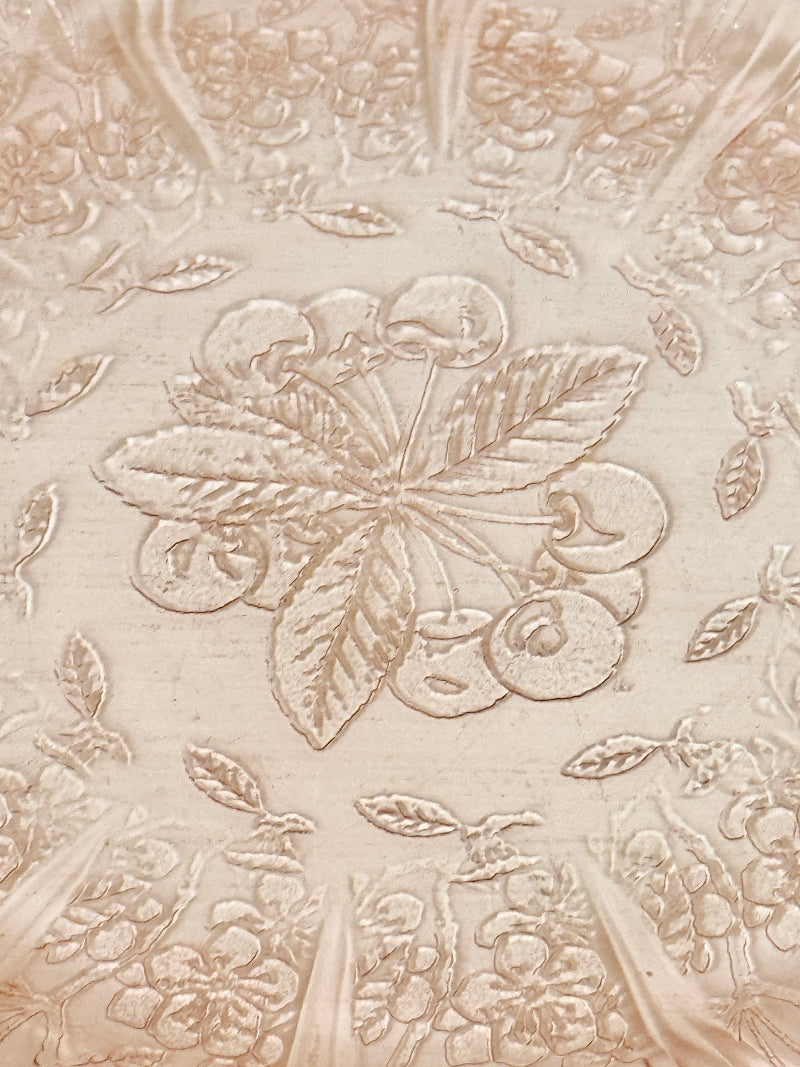 Vintage blush pink pressed glass plate with floral pattern photographed on a white surface