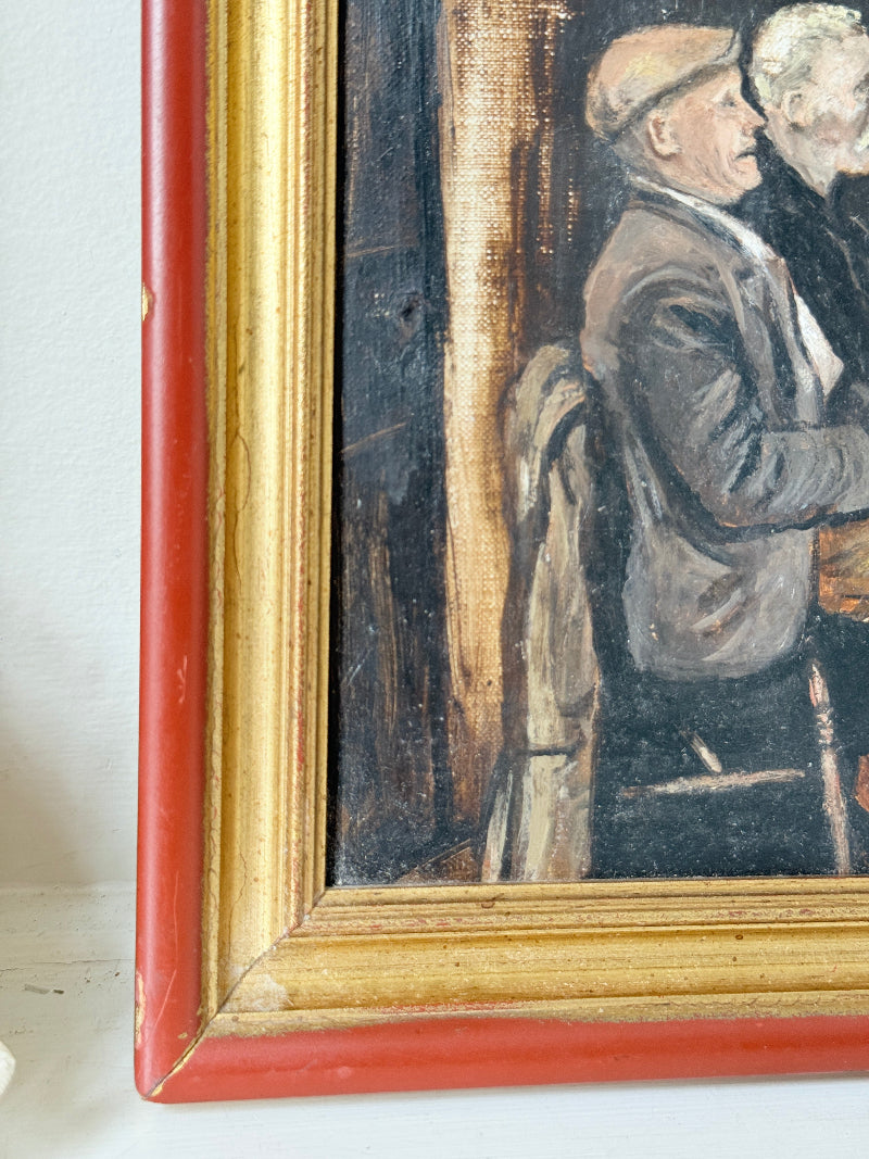 Close-up of a framed painting showing part of a seated figure in a brown jacket and beige hat, with a red and gold painted frame against a light wall.