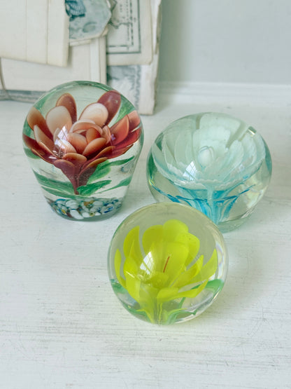 Trio of vintage glass paperweights with red flower, yellow flower and turquoise swirl decoration in clear coloured glass