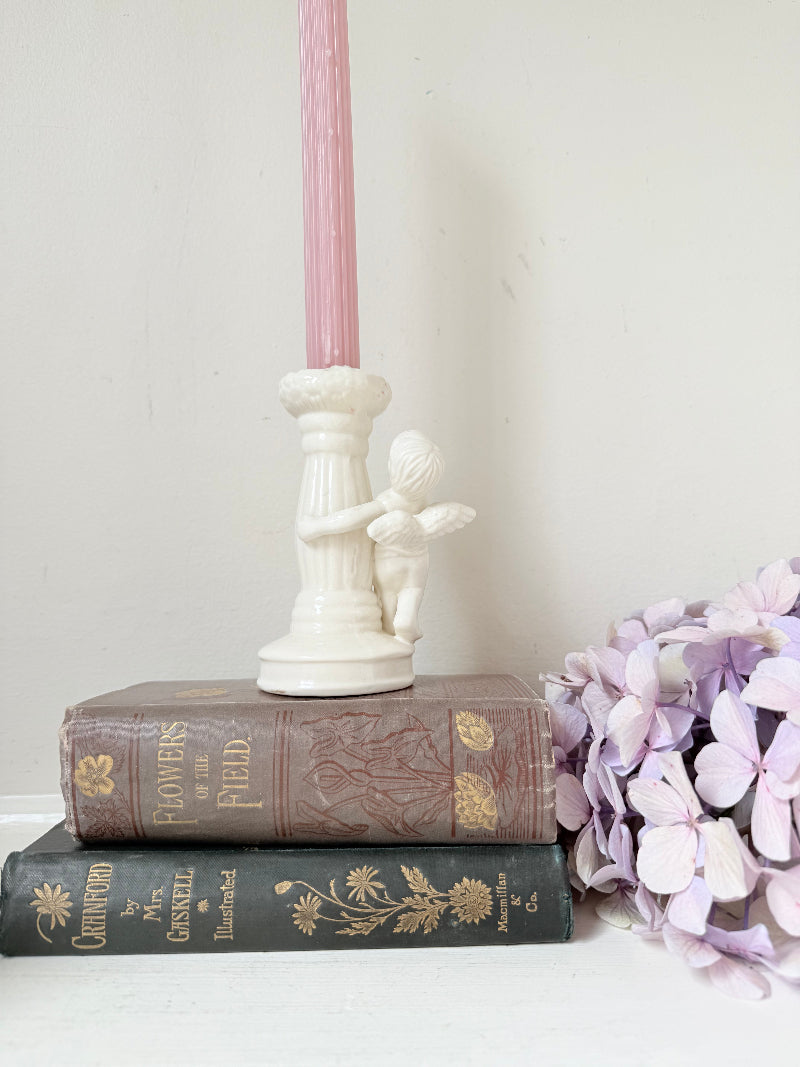 Vintage ceramic candlestick with angel figure and fluted column, cream glazed, styled with pink candle on white surface