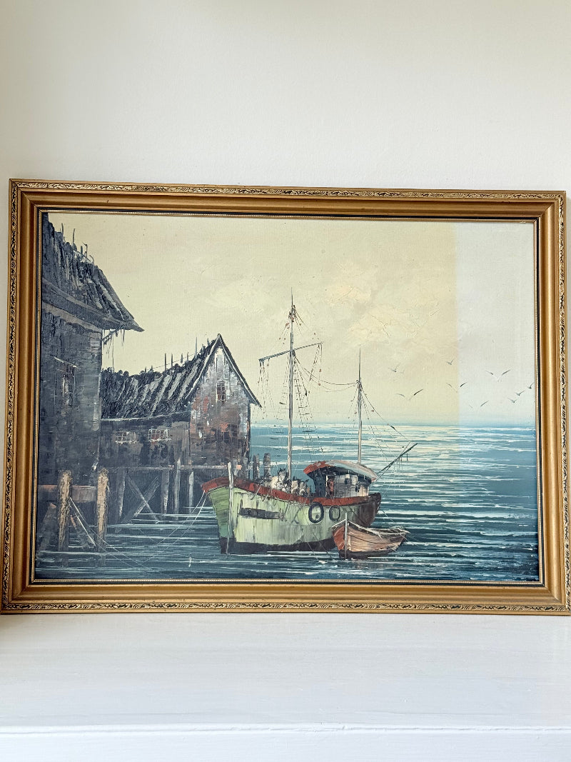 Vintage harbour scene oil painting of fishing boat and wharf buildings in gilt frame, textured brushwork, on white surface.