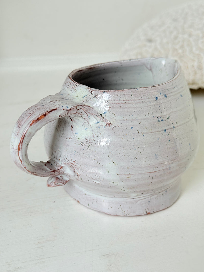 Studio pottery milk jug with soft pink and grey speckled glaze, photographed on a white surface