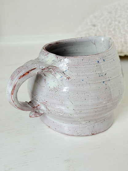 Studio pottery milk jug with soft pink and grey speckled glaze, photographed on a white surface