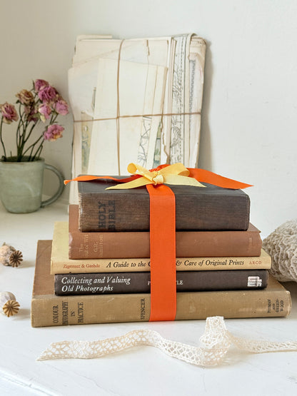 Vintage decorative book bundle in orange and brown with aged hardback covers and bright orange ribbon for shelf styling
