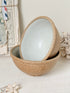 Two stacked ceramic bowls with a speckled beige exterior and a pale mint-green glazed interior, styled on a white tabletop with dried flowers and a vintage postcard frame in the background.