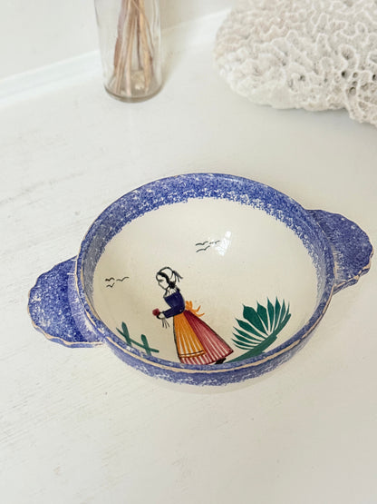 Quimper faience olive bowl with Petit Breton figure and blue speckled rim photographed on a white surface