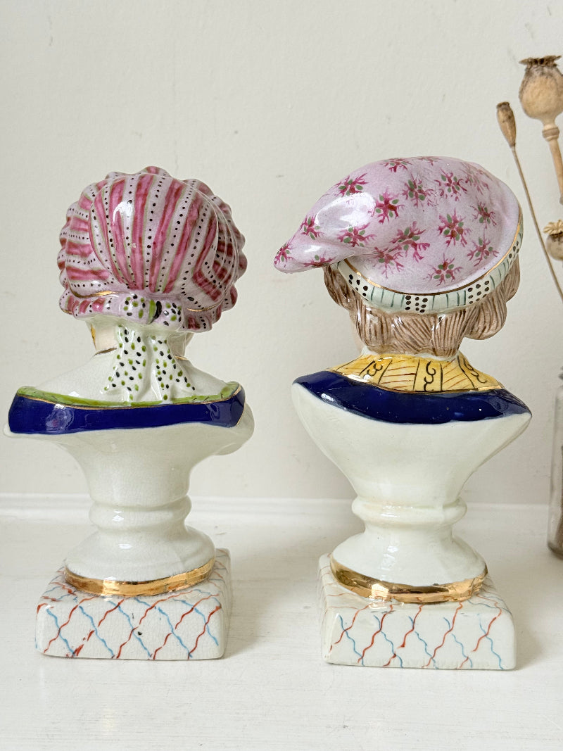 Hand painted Victorian Staffordshire ceramic children busts on white surface, photographed beside dried stems.