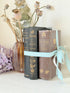 Bundle of antique books with decorative spines tied with ribbon, styled on white surface with dried flowers