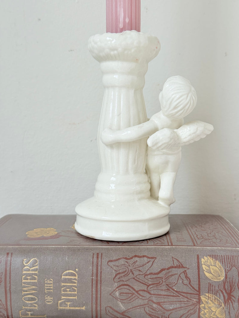 Vintage ceramic candlestick with angel figure and fluted column, cream glazed, styled with pink candle on white surface