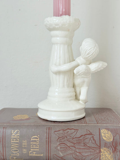 Vintage ceramic candlestick with angel figure and fluted column, cream glazed, styled with pink candle on white surface