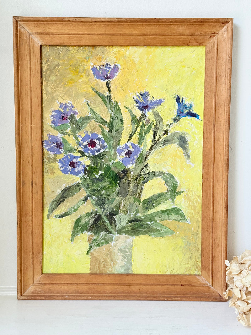 Vintage oil painting of cornflowers in a vase with yellow background in wooden frame photographed on a white surface