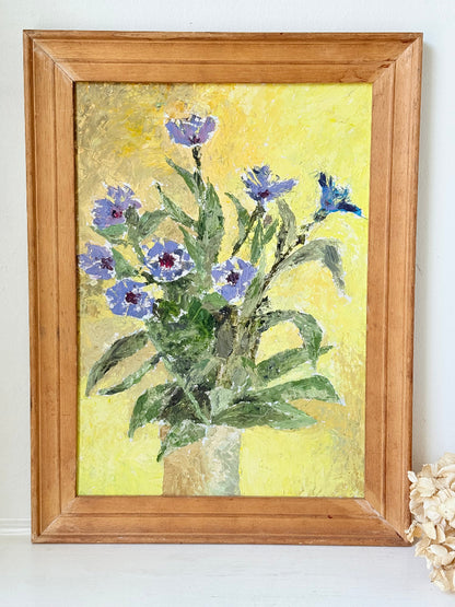 Vintage oil painting of cornflowers in a vase with yellow background in wooden frame photographed on a white surface
