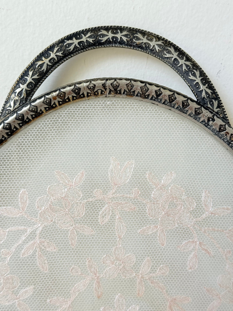 Vintage oval metal tray with pierced gallery sides, twin handles, and floral centre, photographed on white surface.