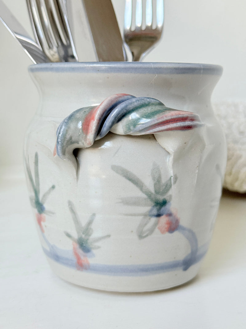 Vintage studio pottery utensil pot with hand painted floral decoration and applied handle detail, photographed on a white surface