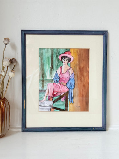 Vintage bright watercolour portrait of a seated woman in pink hat and dress with blue jacket, framed in blue wood with off-white mount, photographed on a white surface.