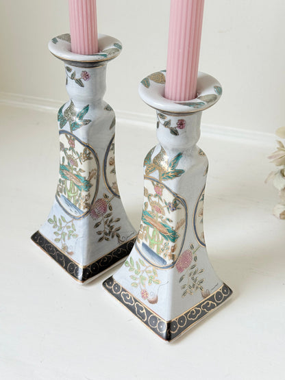Pair of porcelain candle holders with hand-painted floral and vase motif in muted greens, pinks, and gold, styled with blush pink taper candles.