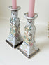 Pair of porcelain candle holders with hand-painted floral and vase motif in muted greens, pinks, and gold, styled with blush pink taper candles.