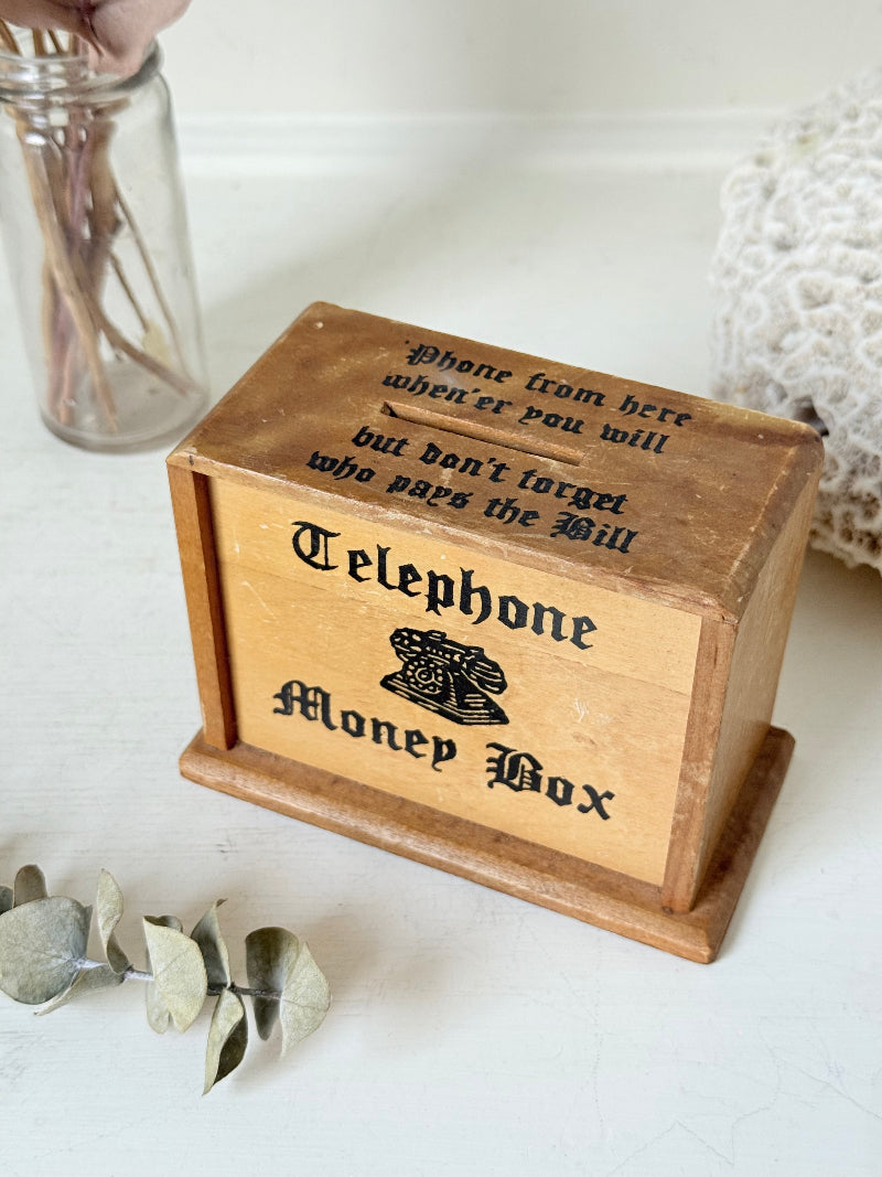 Vintage wooden telephone money box with printed lettering, photographed on a white surface