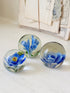 Trio of vintage glass paperweights with hand worked blue floral detail, clear glass domes and green leaf decoration
