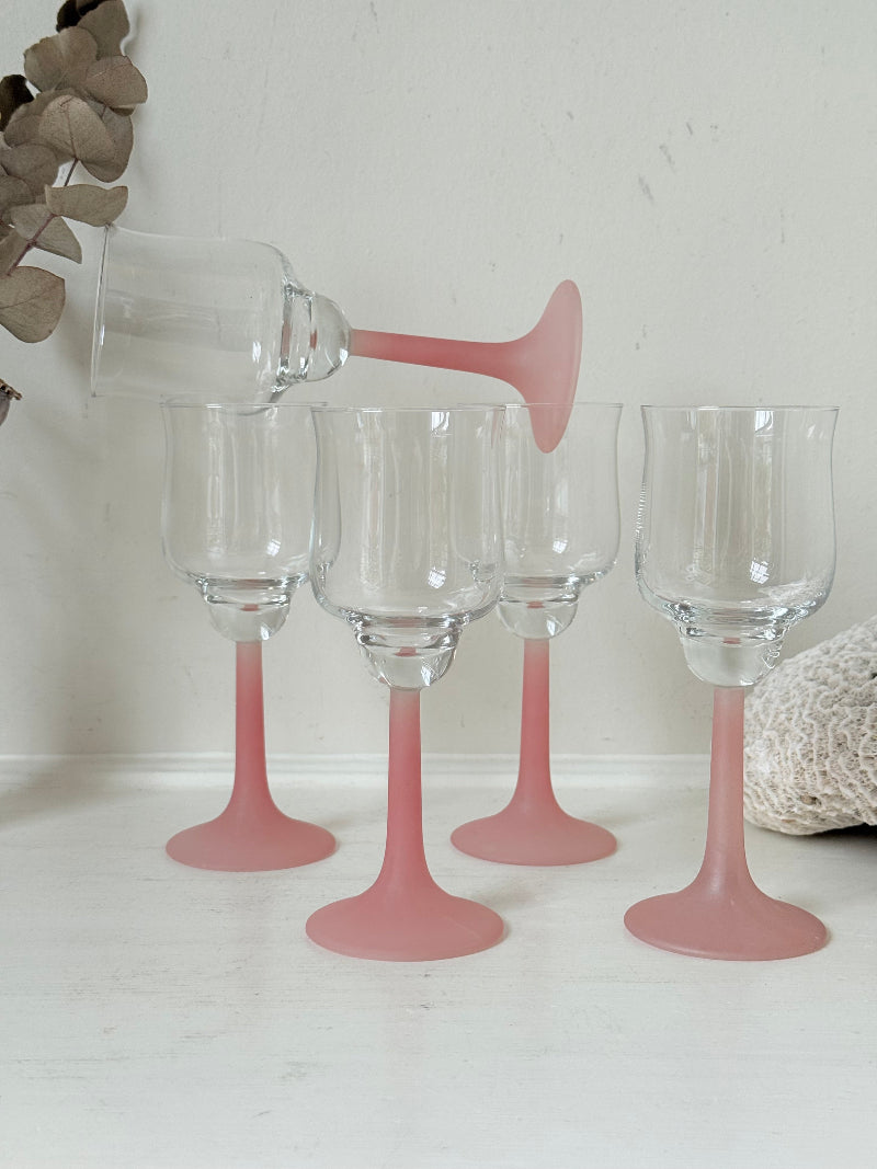 Set of five vintage wine glasses with clear bowls and pink stems photographed on a white surface.