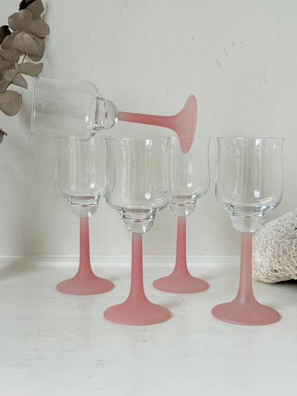 Set of five vintage wine glasses with clear bowls and pink stems photographed on a white surface.