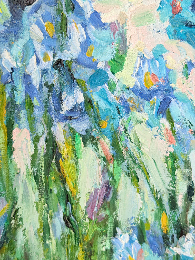 Framed impressionist-style oil painting of blue irises and garden scene, photographed on a white surface