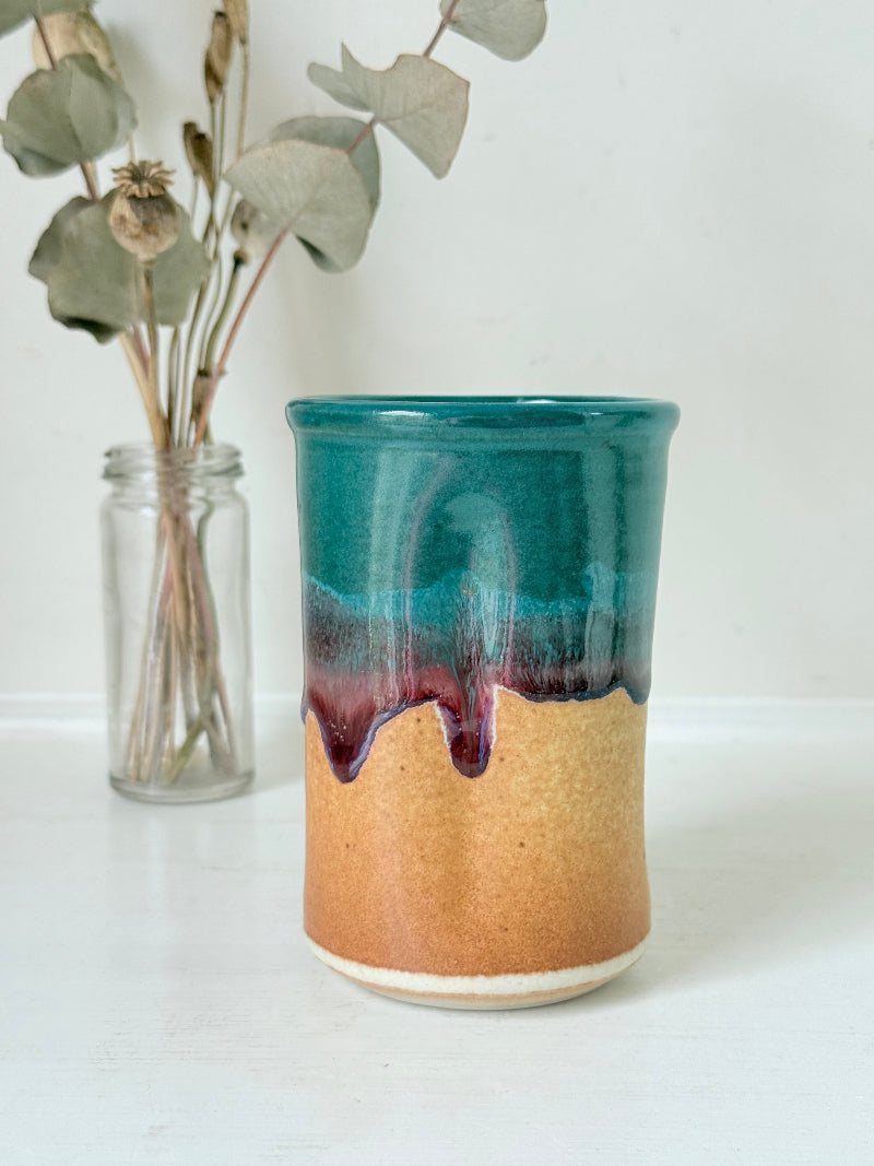 Studio pottery pen pot with teal and plum drip glaze, photographed on a white surface
